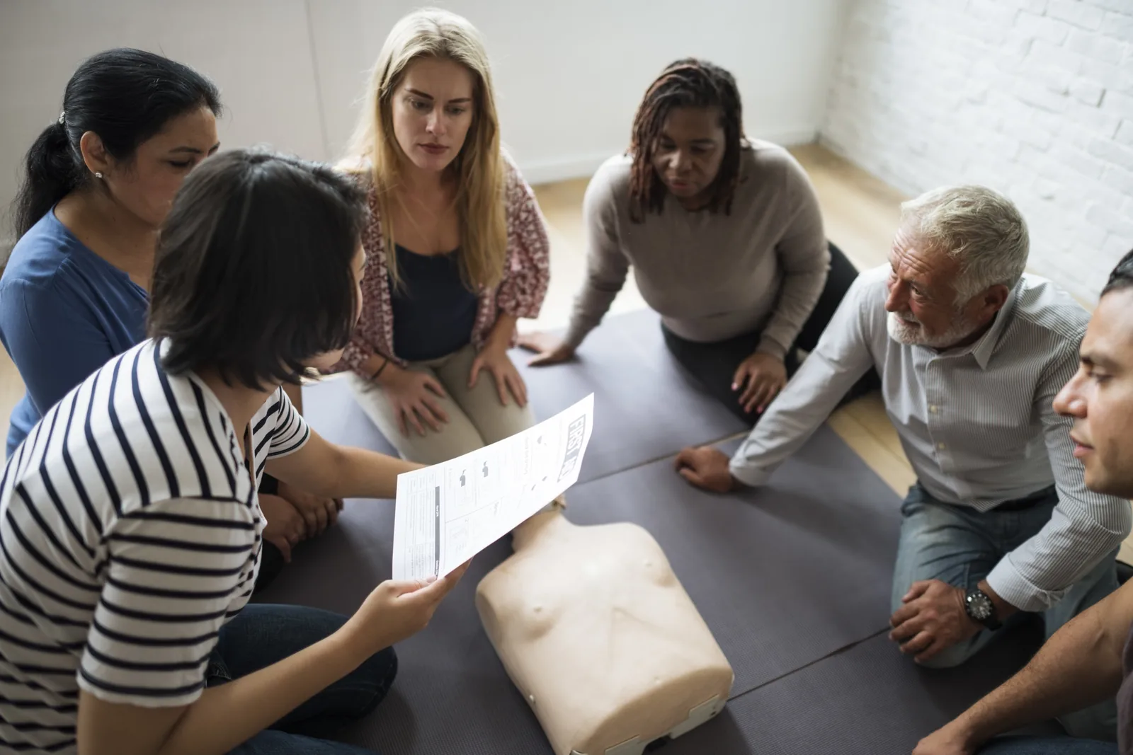 Adults gathered around a CPR manikin during first-aid training